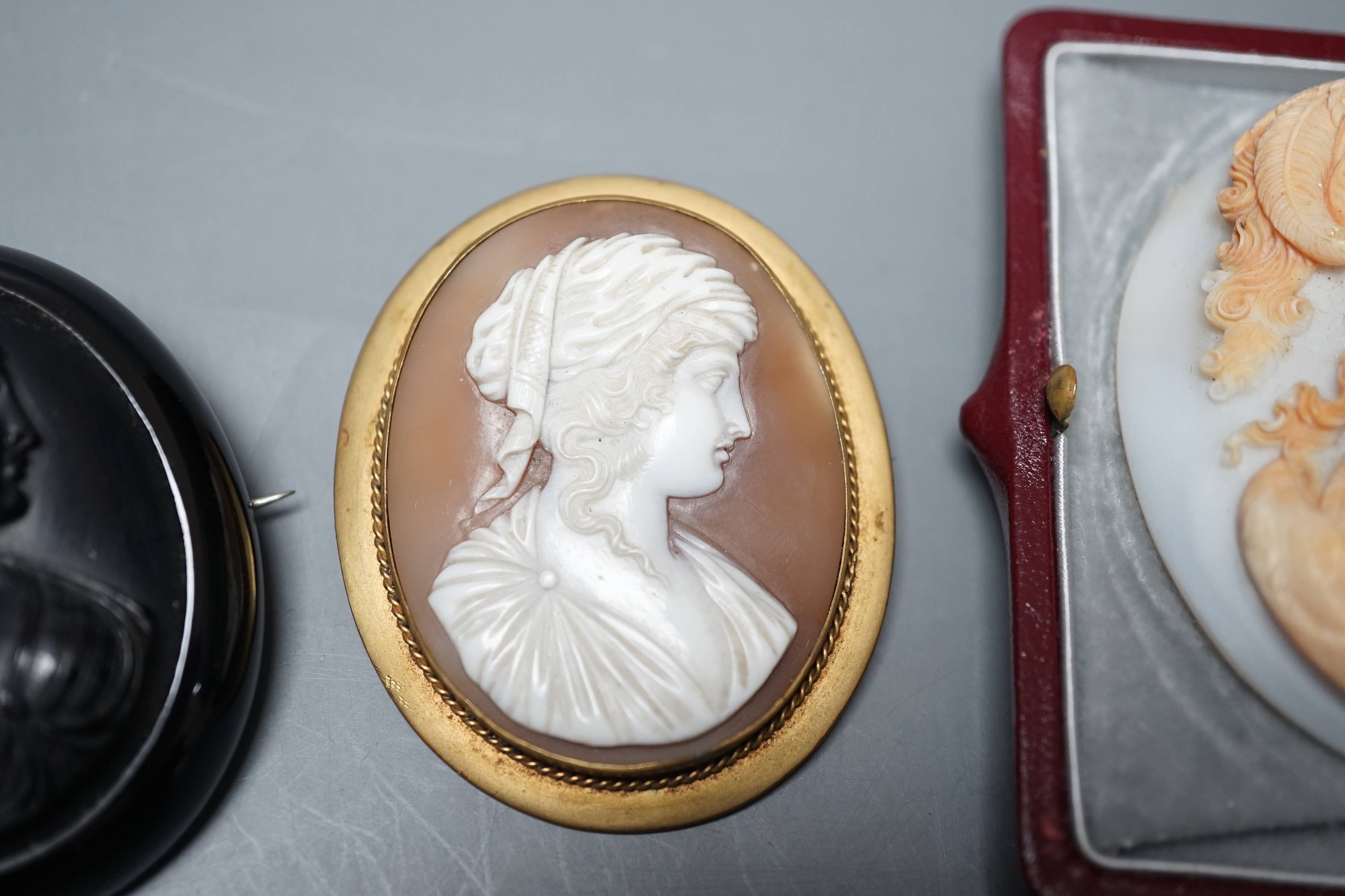 A good quality unmounted oval cameo shell, carved with the bust of a Roman soldier to sinister, 56mm, in Antrobus box, together with two cameo set brooches.